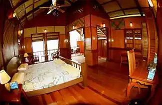 Spacious interior of a luxury overwater chalet at Kapalai Resort, with warm wooden walls, a vaulted ceiling, and a comfortable double bed.