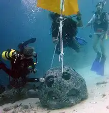 Scuba divers participating in a marine conservation project at Mataking Island, carefully deploying a concrete reef ball to encourage new coral growth.