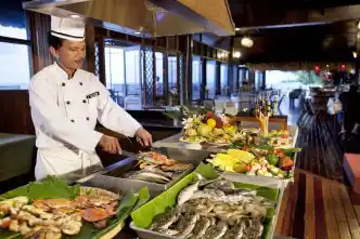 Resort chef grilling fresh-caught seafood, including fish and crabs, at a live cooking station in the Mataking Island Resort restaurant.