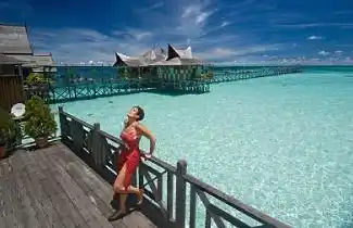 Guest enjoying the brilliant sunshine on a private balcony at Mabul Water Bungalows, overlooking the resort's stunning turquoise lagoon.