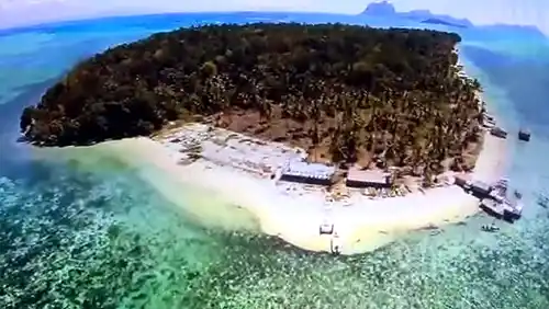 This island is part of a protected marine park. Aerial view of Pulau Sebangkat in the Tun Sakaran Marine Park, showing its sandy shores, lush interior, and surrounding turquoise reefs.