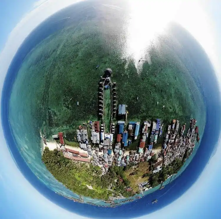 Unique 360-degree drone view of the Billabong Scuba dive lodge and Mabul's sprawling water village, surrounded by vibrant shallow reefs and the deep blue sea.
