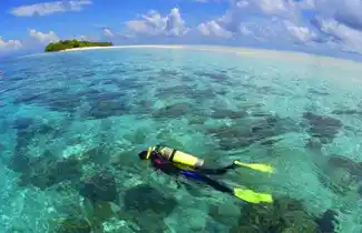 Scuba diver gliding over a shallow, sunlit coral reef in the crystal-clear waters surrounding Mataking Island, a 5-star luxury PADI resort.