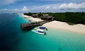 Aerial view of the arrival jetty at Mataking Island Dive Resort, with dive boats moored in turquoise water next to the perfect white sand beach.