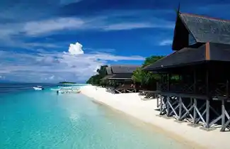 Idyllic private beach at Pulau Mataking, with luxury chalets lining the pristine white sand and crystal-clear turquoise water of the Celebes Sea.