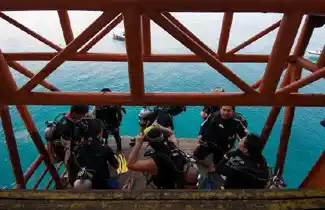 Scuba divers riding the unique platform lift at Seaventures Dive Rig, being lowered directly from the rig into the water for their dive.