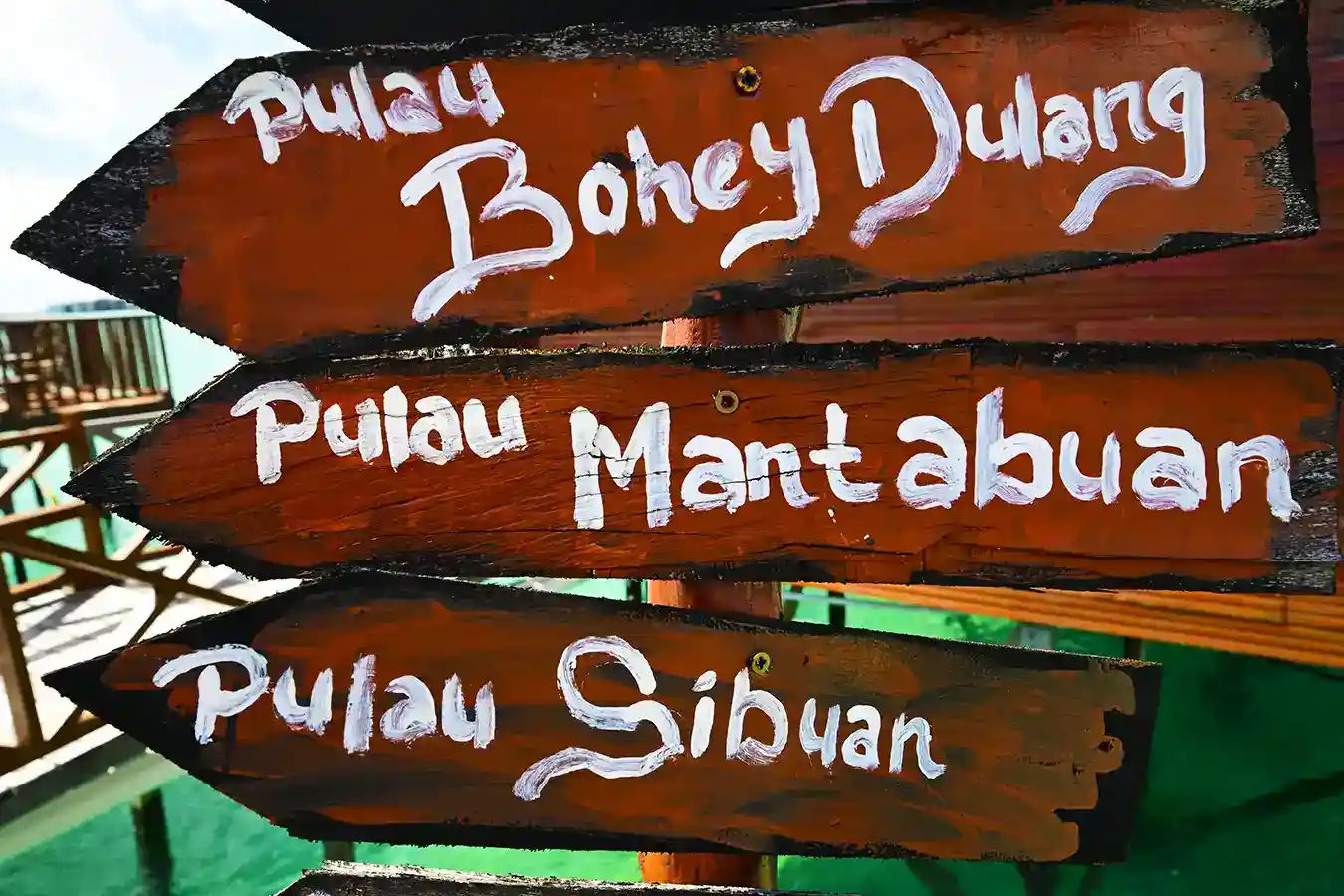 Hand-painted wooden signpost indicating the directions to the famous island hopping destinations of Pulau Bohey Dulang, Mantabuan, and Sibuan.