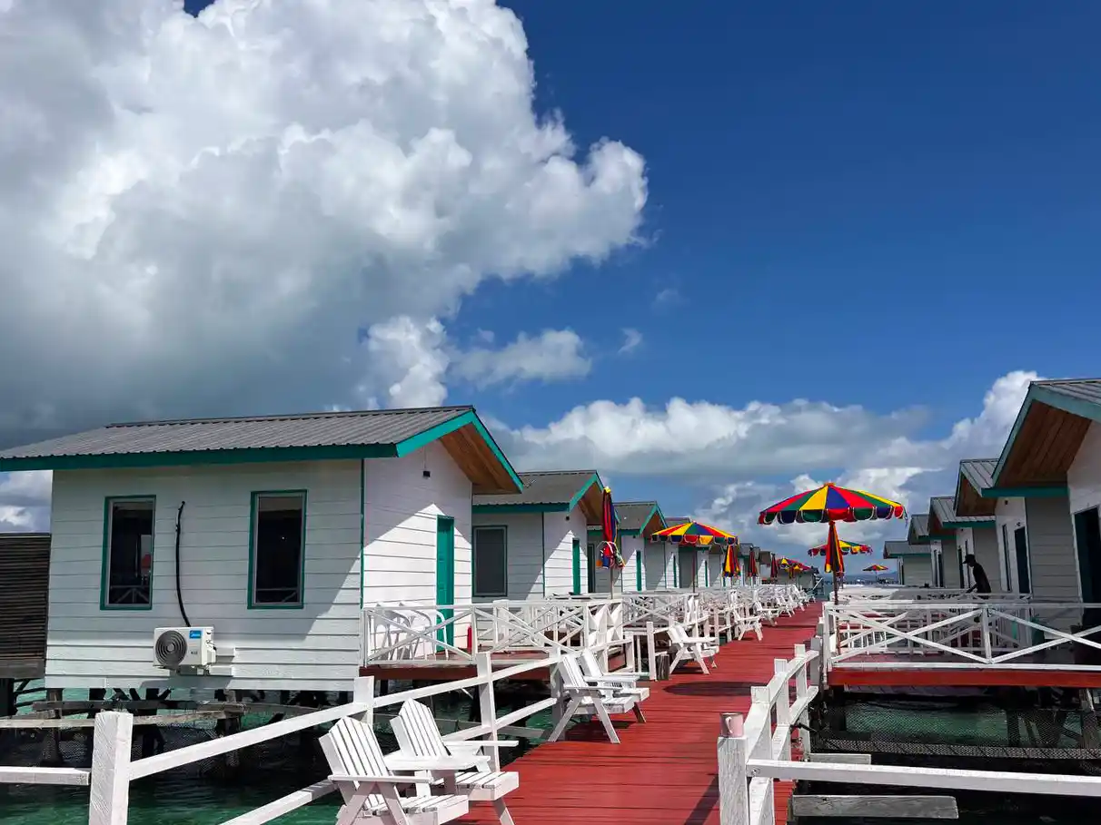 Cheerful white overwater chalets with colorful umbrellas lining the red boardwalk of the Blue Ocean Resort near Semporna on a perfect sunny day.