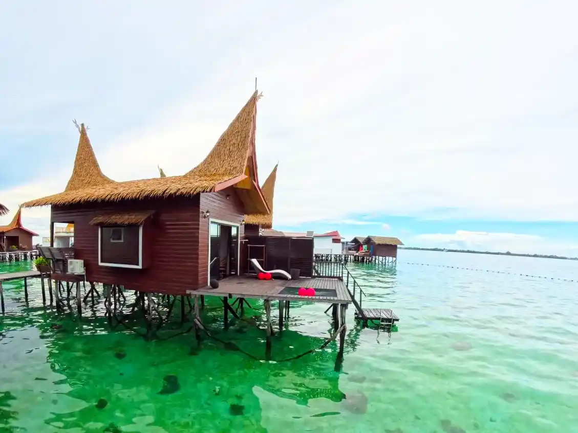 Private overwater chalet at Dayang Resort, featuring traditional thatched-roof architecture and a sundeck with direct stair access into the turquoise sea.