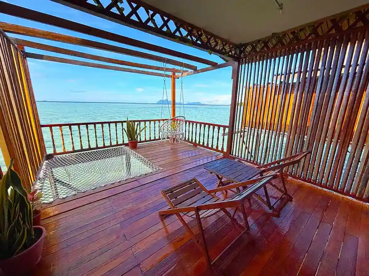 Incredibly relaxing private balcony at Larapan Water Village, featuring an over-water net hammock and a hanging swing with panoramic sea views.