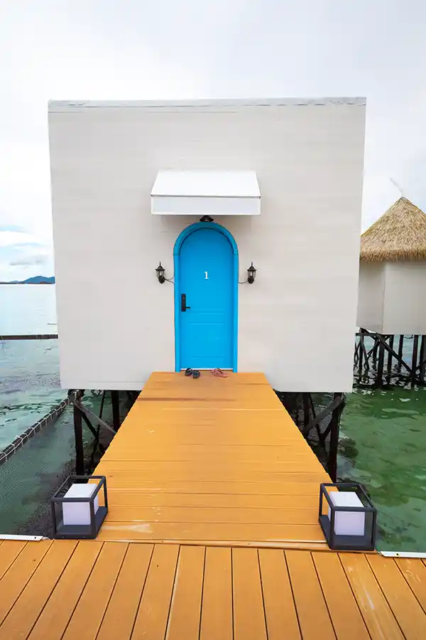 Striking minimalist design of an overwater chalet at Royal Resort Semporna, with a vibrant blue door creating a beautiful color contrast.