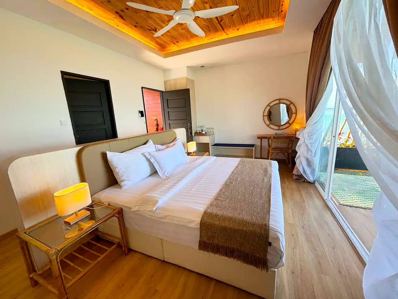 Bright and beautifully designed bedroom at Sand Bay Resort, with a unique wood-paneled ceiling and sliding glass doors that open onto a private balcony.
