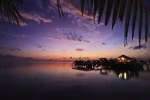 Spectacular purple and orange sunset over a Sipadan water village resort, with lights from the jetty reflecting on the calm sea.