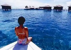 A woman guest enjoys the breathtaking view of Kapalai Dive Resort's iconic overwater bungalows while gliding across the crystal-clear turquoise sea near Sipadan, Sabah, Borneo.