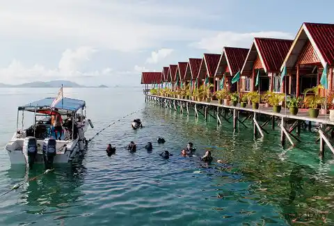 A popular and affordable base for Mabul diving. Scuba divers in the water preparing for a dive right off the jetty of Uncle Chang's dive lodge, a popular backpacker resort on Mabul island.
